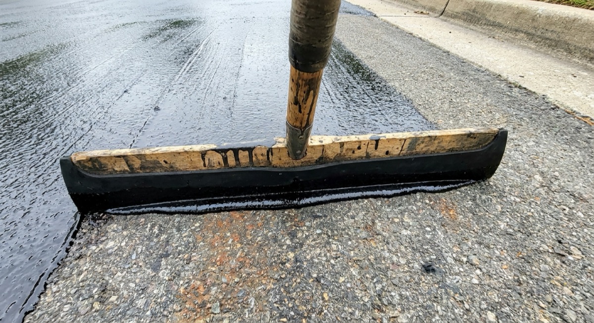 Sealcoat being squeegeed onto a new blacktop driveway for protection